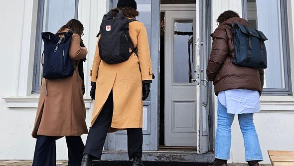 Tre personer går uppför en trappa in i ett hus 